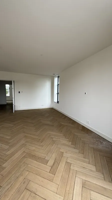 Woonkamer met strak afgewerkte witte wanden na renovatie, project Haarlem