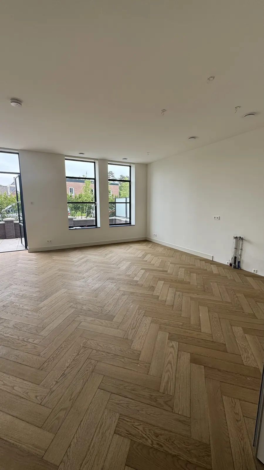 Afgewerkte woonkamer met witte wanden en visgraatvloer, project Haarlem