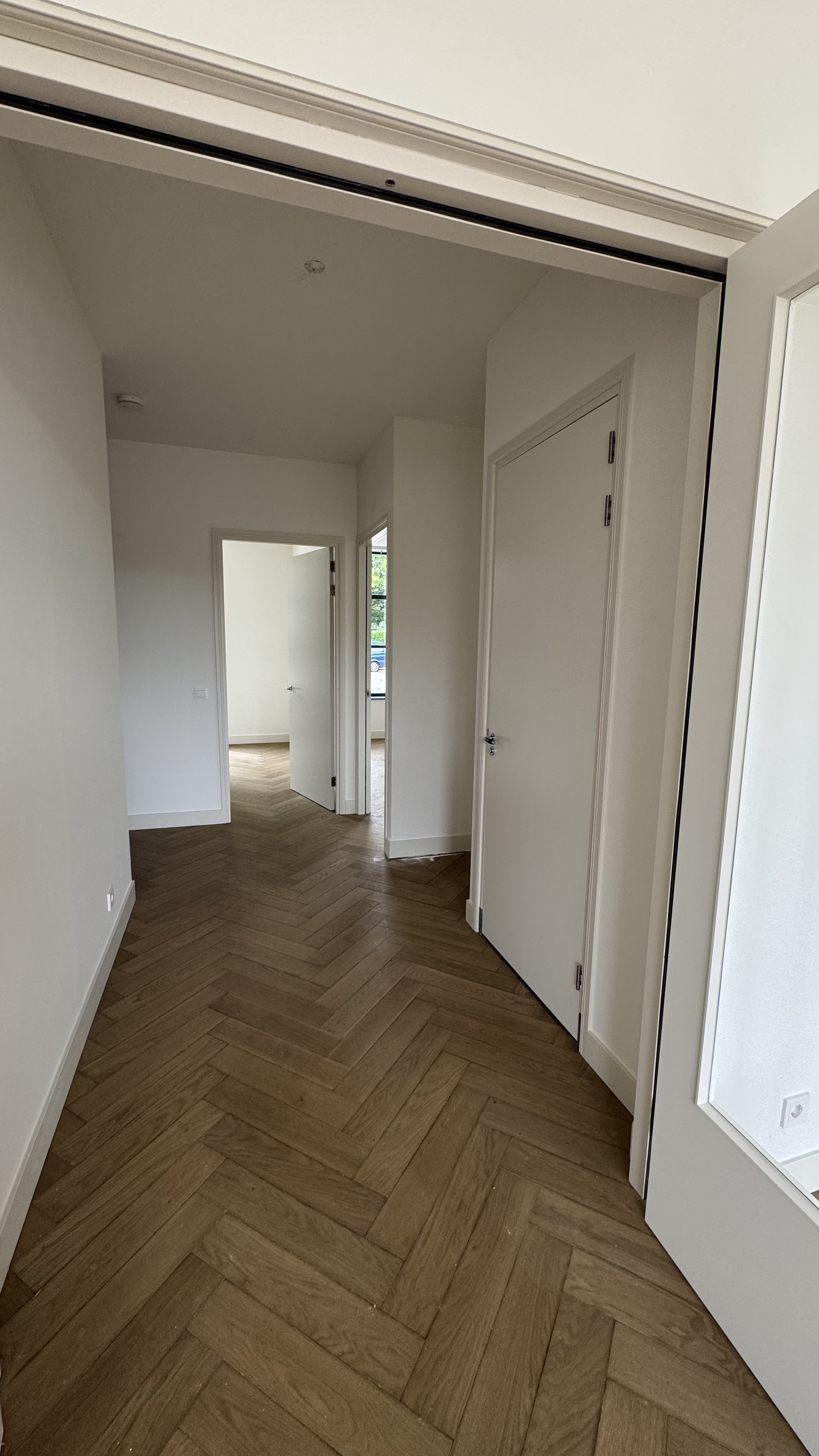 Hal met strakke witte muren en visgraatvloer na renovatie Haarlem